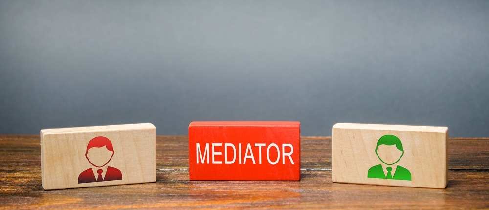 Why choose mediation services London_blog image_wooden blocks with the word mediator in the middle and one wooden block of red and green to the left and right each inscribed with the head and shoulder of a man in a suit